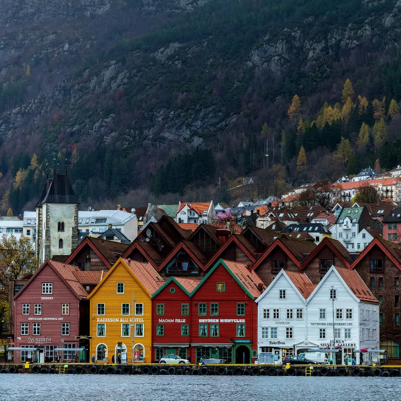 Historic wooden buildings in Bryggen, Bergen, Norway, facing the harbour with forested mountains in the background Historic wooden buildings in Bryggen, Bergen, Norway, facing the harbour with forested mountains in the background