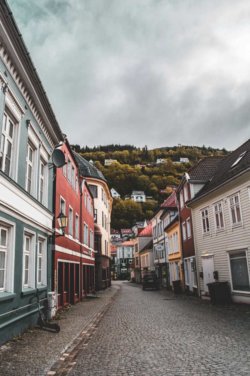 Quiet cobblestone street in Bergen, Norway, lined with colourful wooden houses and hillside homes in the background under an overcast sky Quiet cobblestone street in Bergen, Norway, lined with colourful wooden houses and hillside homes in the background under an overcast sky